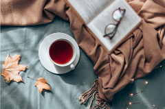 Book with glasses, warm cup of tea and a brown throw blanket